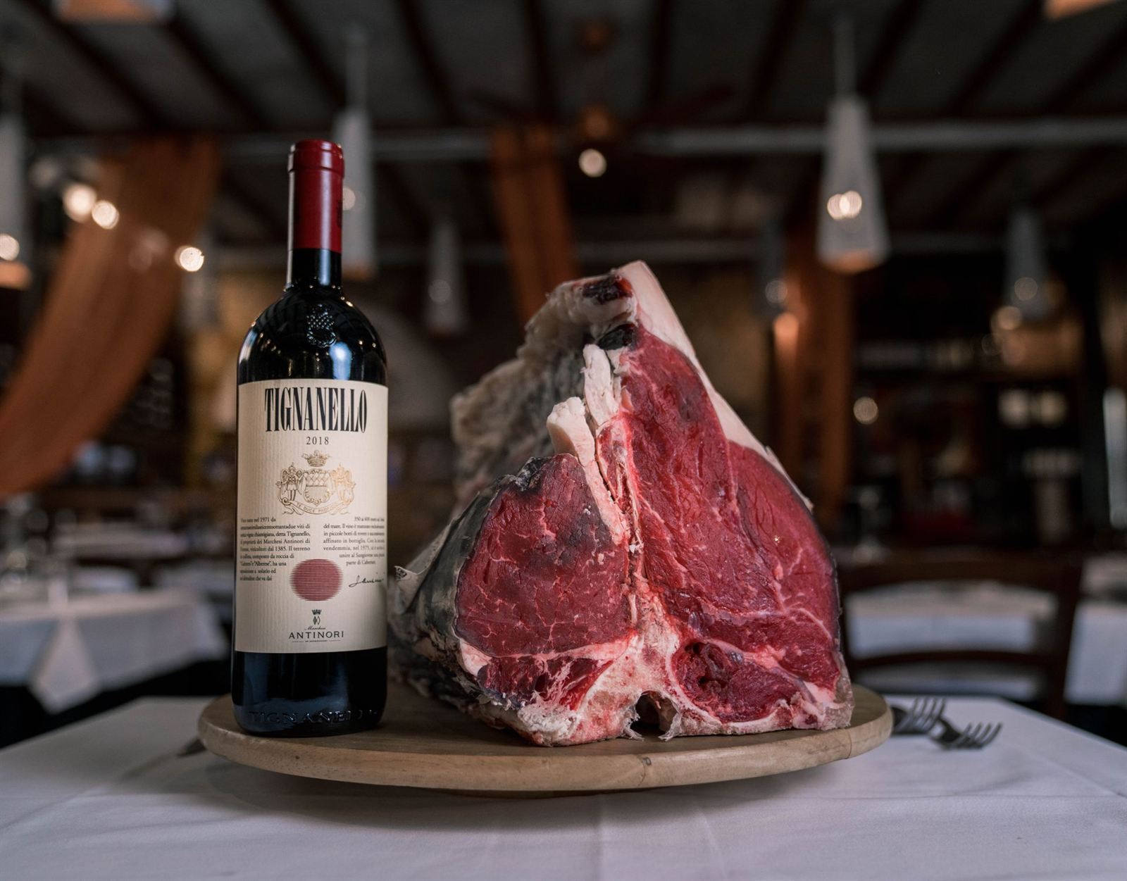 Côte de bœuf maturée posée sur un plateau en bois, à côté d'une bouteille de vin rouge