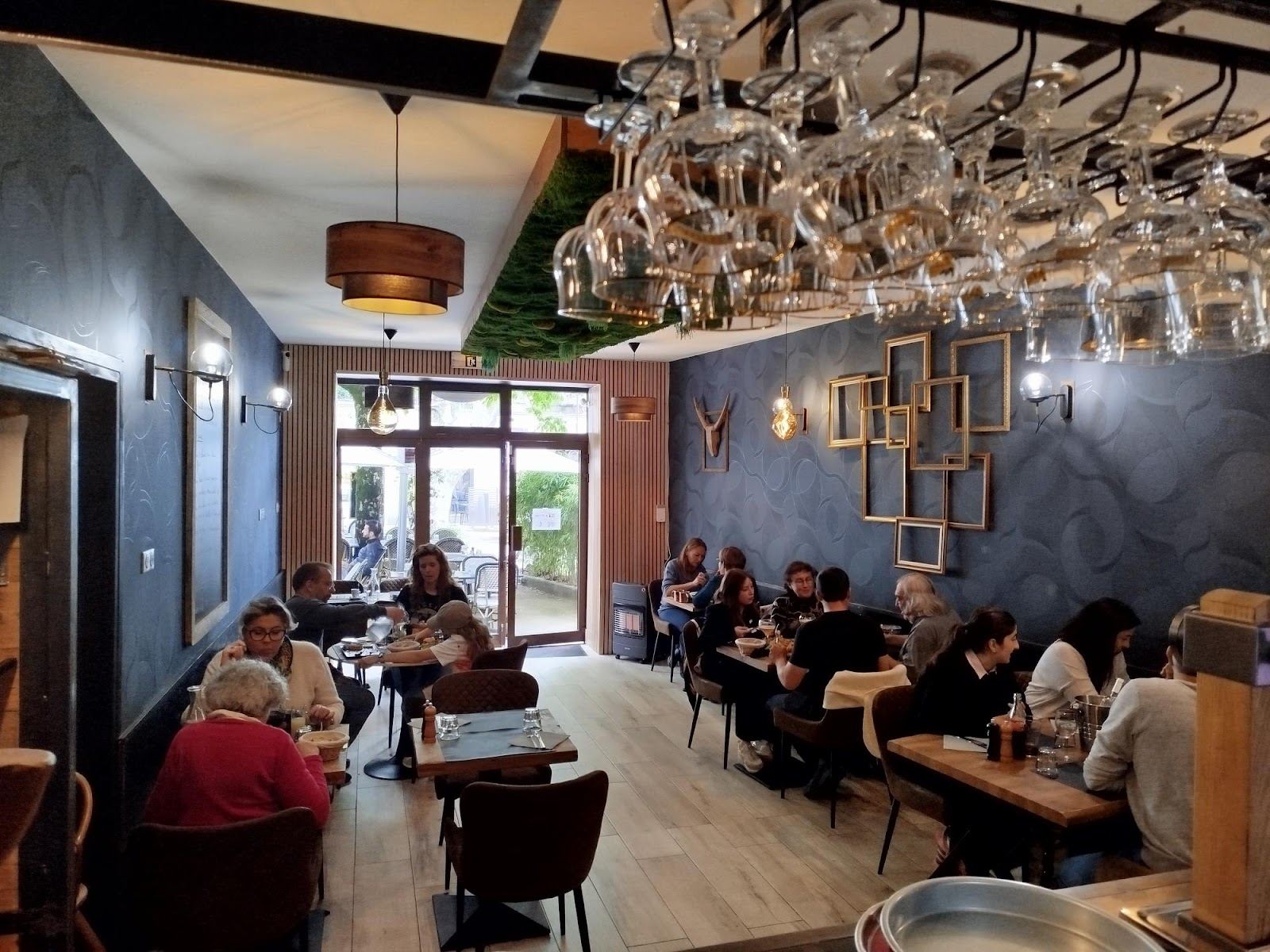 La salle du restaurant : murs ardoise, verres suspendus au plafond, tables en bois